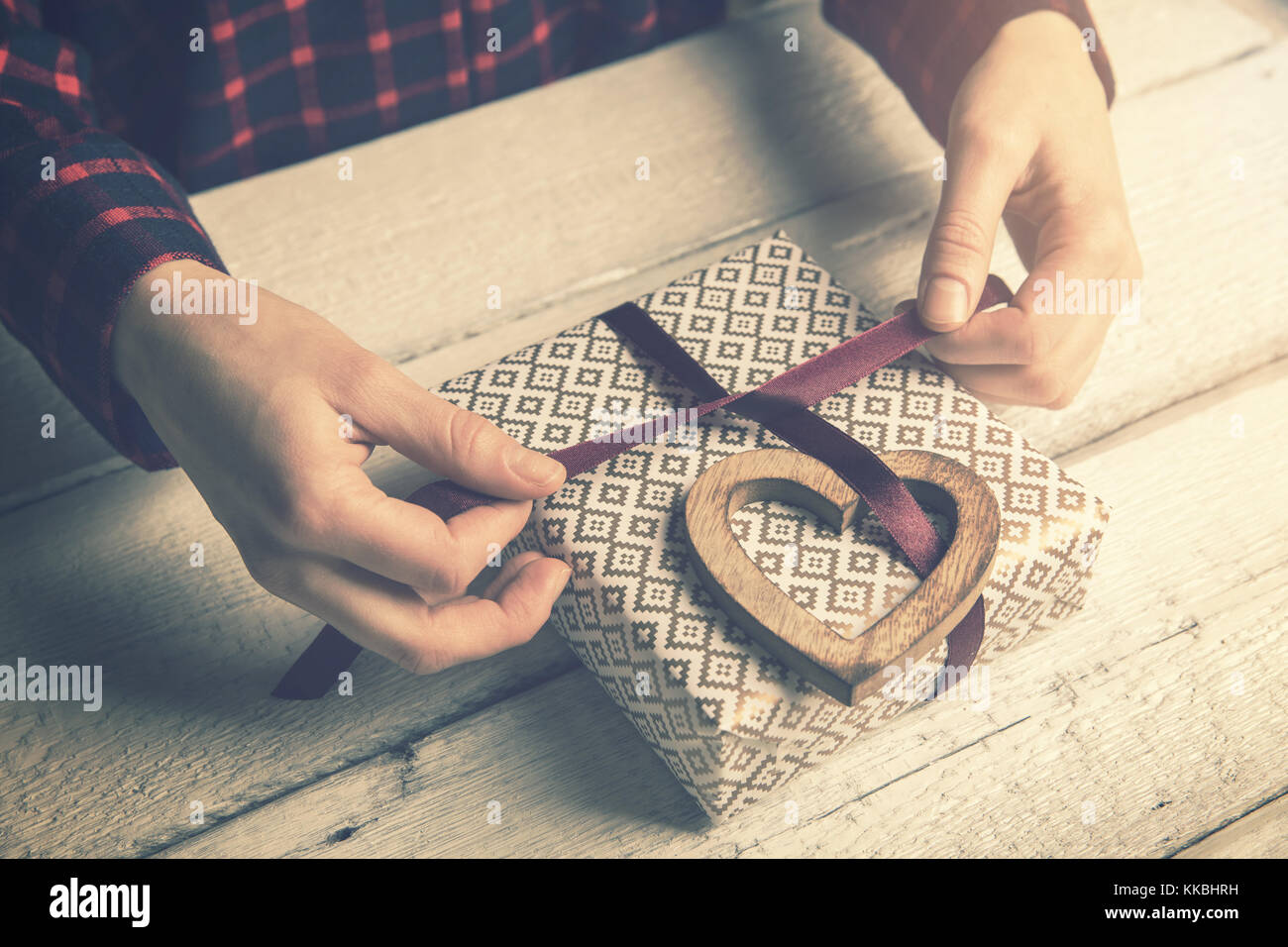 Frau wickeln ein Geschenk für die Lieben. das Binden einer Schleife mit Herzen aus Holz Dekor Stockfoto