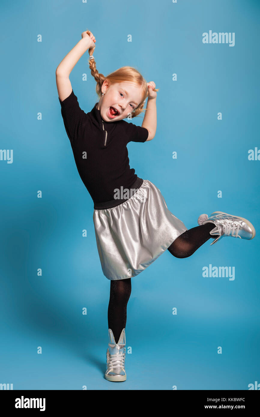 Kleines Mädchen mit Zöpfen in stilvoller Kleidung auf blauem Hintergrund Stockfoto