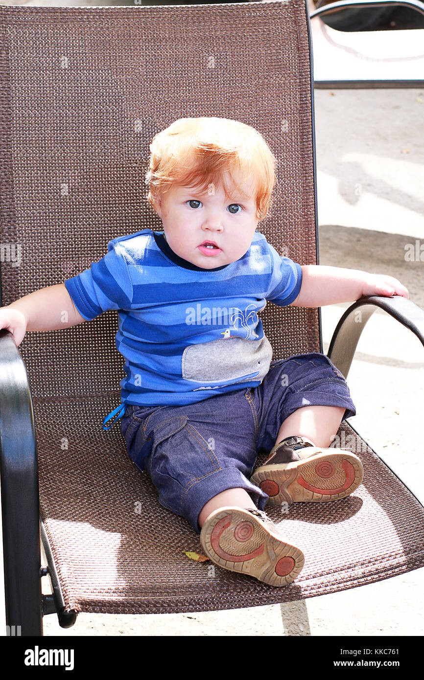 Ingwer Toddler mit blauen Augen in Jeans und blaue T-Shirt sitzen auf Open Air im korbstuhl gekleidet. Stockfoto