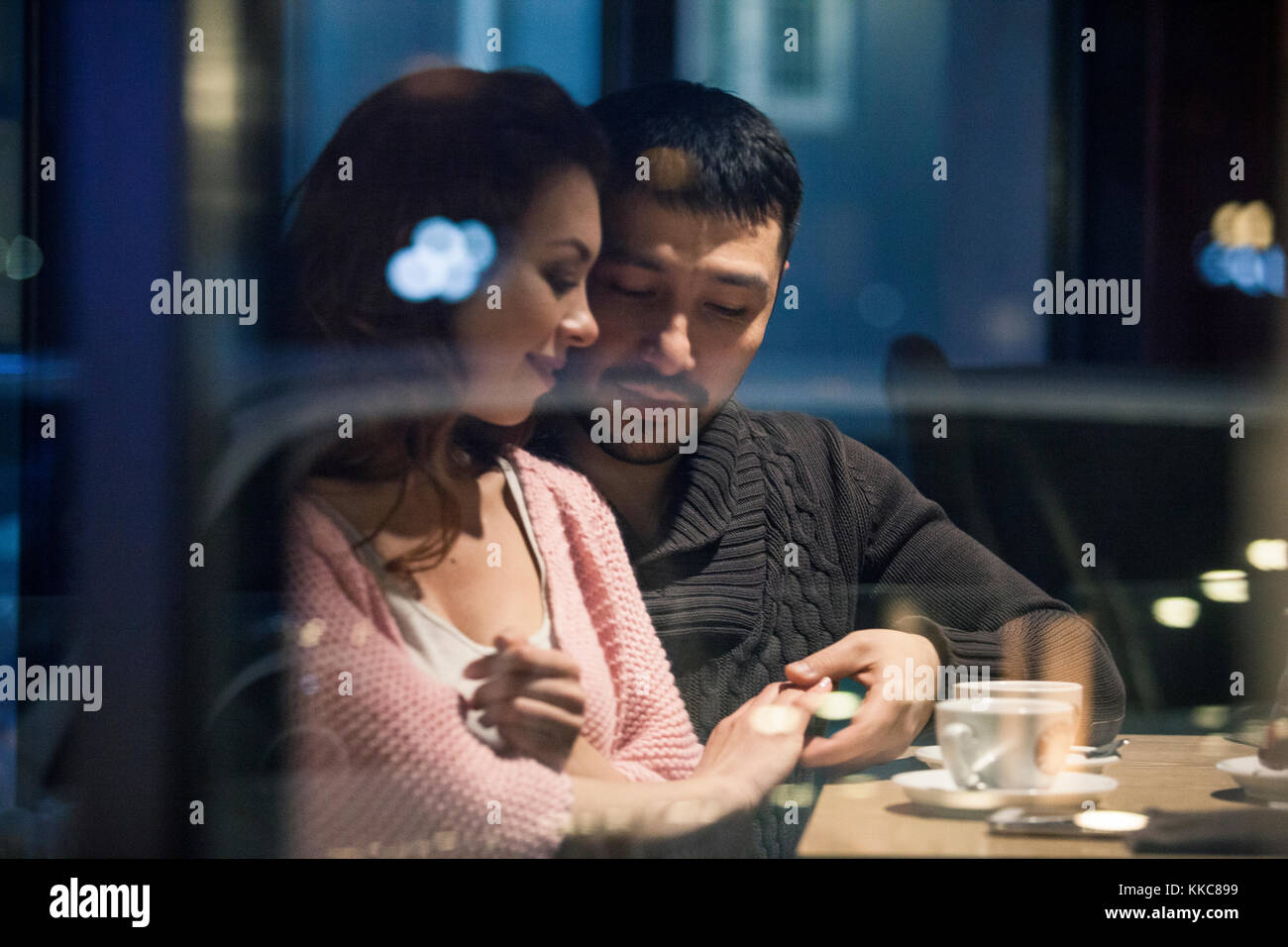Paar durch ein Fenster auf lokaler Kaffee Platz und genießen winter nacht mit heißen Getränken und beiläufiges Gespräch. Schuss von aussen durch den Wind Stockfoto