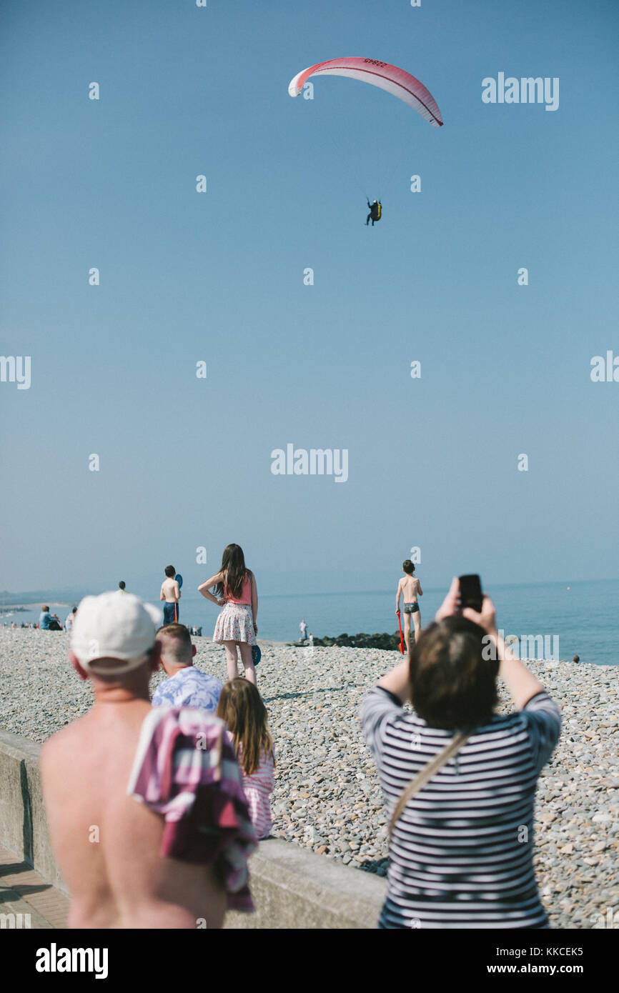 Menschen beobachten Fallschirm Flug über Bray steinigen Strand an einem sonnigen Tag. Bray, Wicklow, Irland Stockfoto