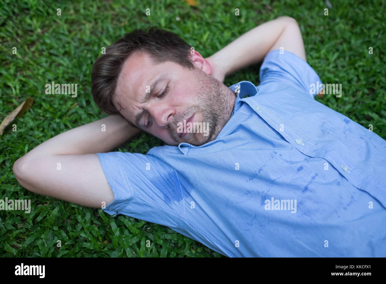 Kaukasier, junger Mann ruht auf grünem Gras und Suchen auf seinem nassen T-shirt. Stockfoto