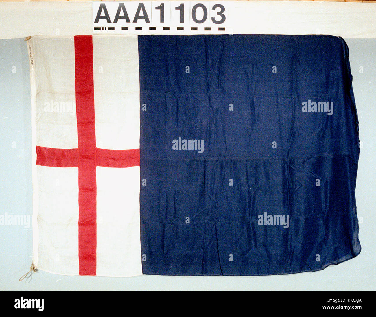 Das Haus Flagge von George Traill und Söhne, London. Die Flagge ist aus Wolle Bunting, Maschine genäht mit einem Hebezeug. Ein Seil und Holz- toggle ist beigefügt. Inschrift: 'T C Hayward & Co". Eine rechteckige Flagge mit der Fliege Ecken abgerundet. Das Feld ist vertikal geteilt. Eine kleinere weiße Fläche an der Hoist Ende hat ein rotes Kreuz. Die fliege Ende ist blau. AAA 1103 House flag, George Trail und Söhne RMG RP -74-24 Stockfoto