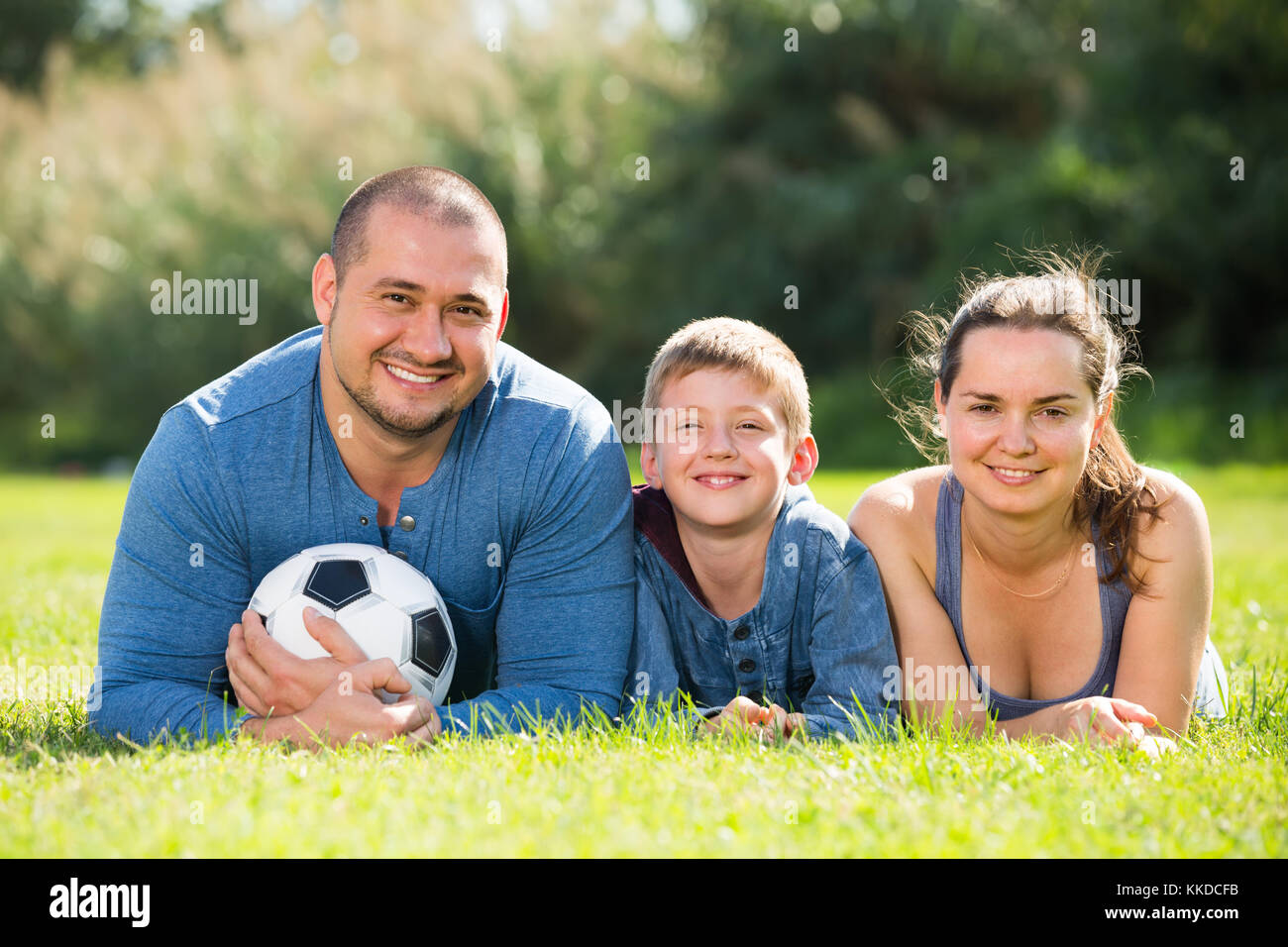 Fröhlich lächelnd, Mutter, Vater und Teenager Sohn im Gras mit Fußball liegen Stockfoto