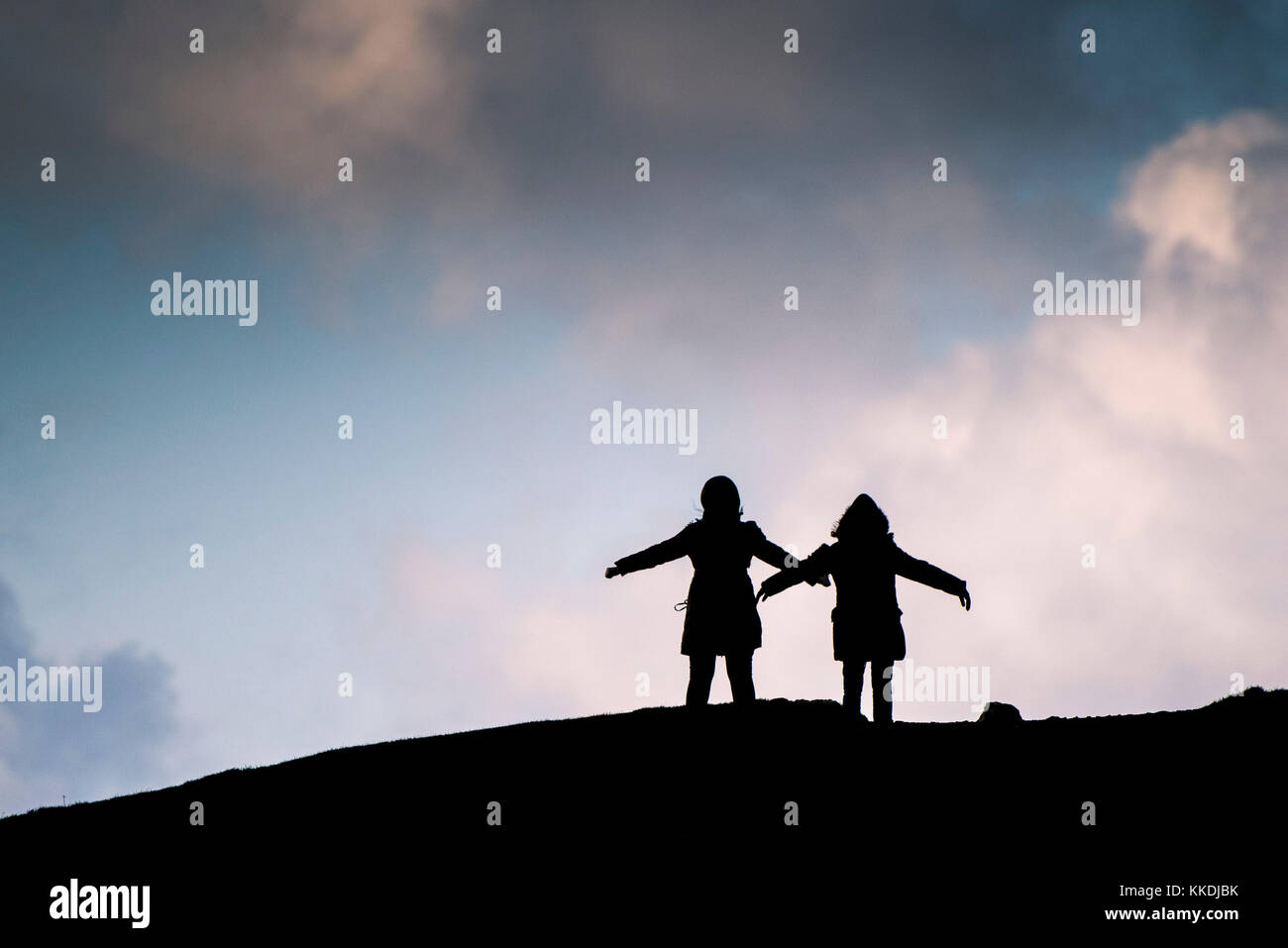 Silhouetten - die Silhouette zweier Menschen, die mit ihren Armen bei starken Winden auf dem Gipfel des East Pentire Newquay Cornwall UK stehen. Stockfoto