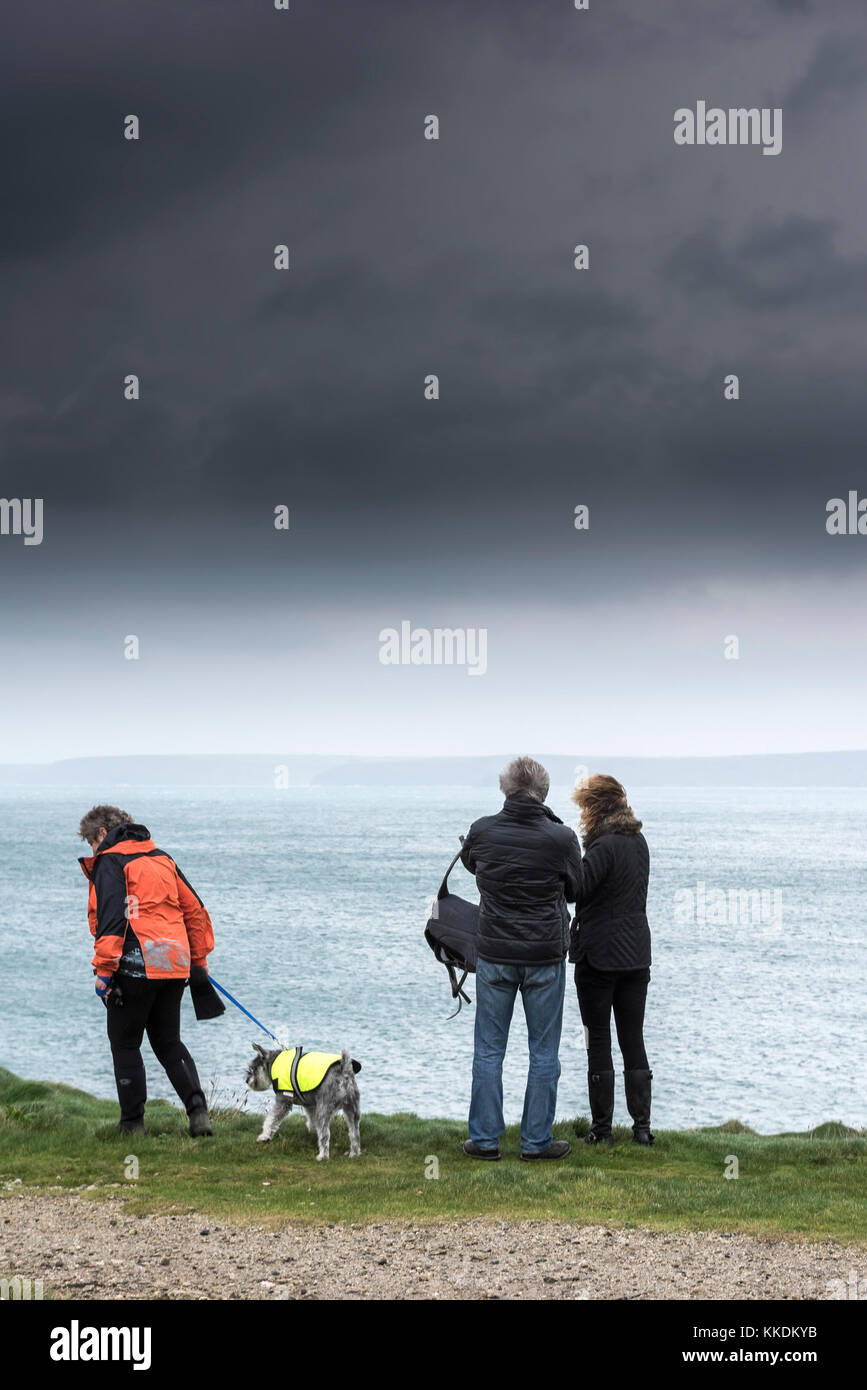 Wetter in Großbritannien - ein Hundespaziergänger und zwei Paare stehen auf den Klippen, die das Meer überblicken, während sich dunkle Sturmwolken Newquay Bay nähern; Cornwall; Großbritannien. Stockfoto