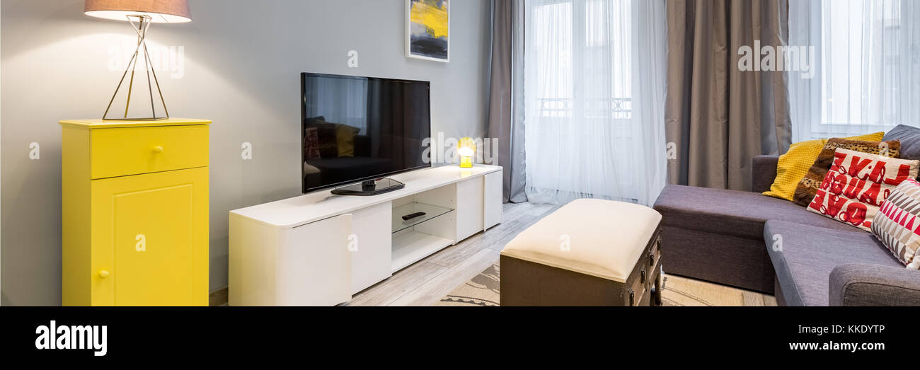 Modernes Wohnzimmer mit tv, Couchtisch und gelbem Schrank, Panoramablick Stockfoto