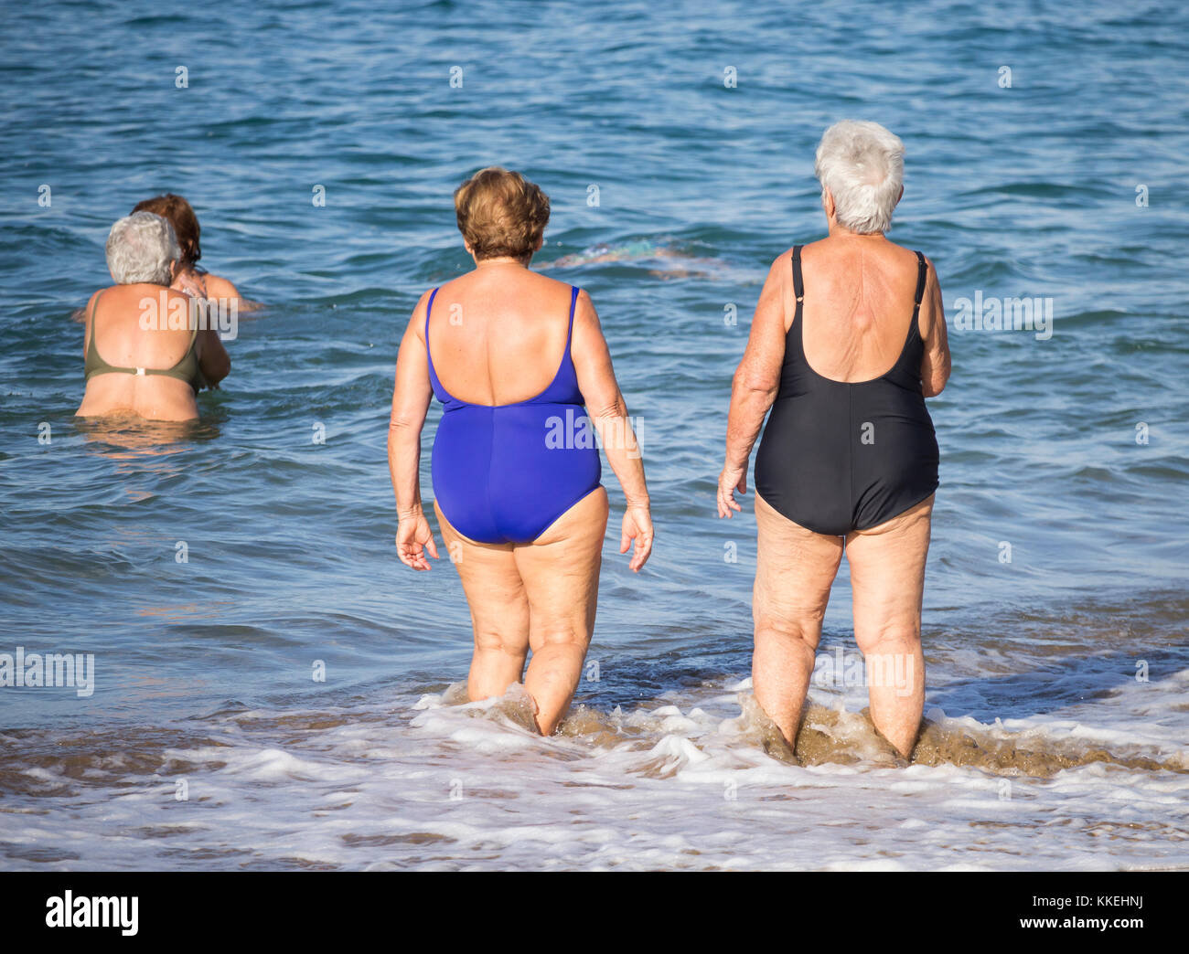 Ältere spanische Frauen, die nach ihrem täglichen Yoga-/Stretching-Kurs am Strand im Meer schwimmen gehen. Stockfoto