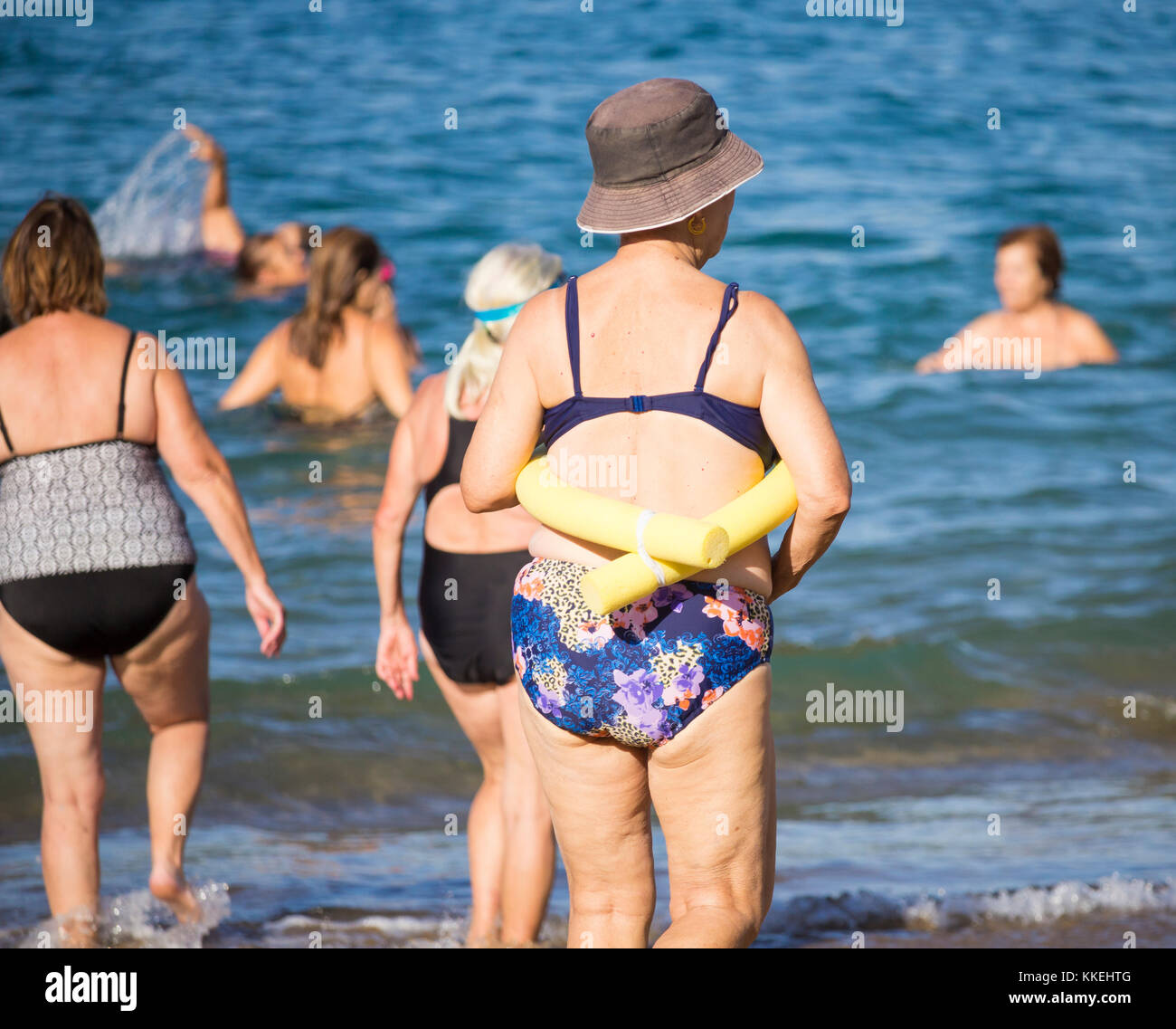 Ältere spanische Frauen, die nach ihrem täglichen Yoga-/Stretching-Kurs am Strand im Meer schwimmen gehen. Stockfoto