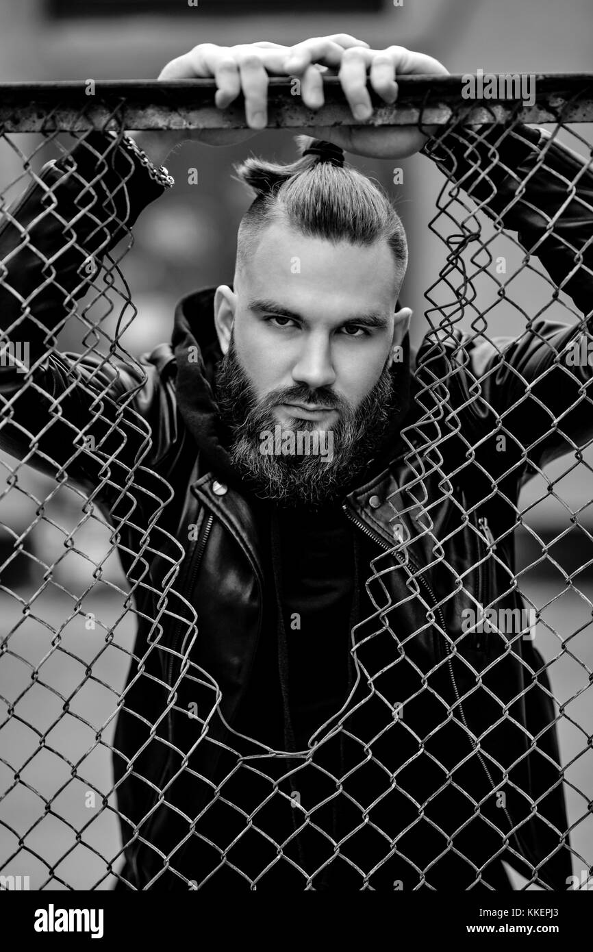 Moderne junge bärtige Mann in Schwarz style Kleidung im städtischen Hintergrund stehen. Stockfoto