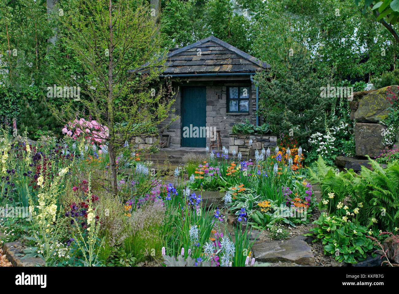 Ein Landhaus und Garten in einem bewaldeten Steingarten mit einer bunten Blütenpracht gelegen Stockfoto