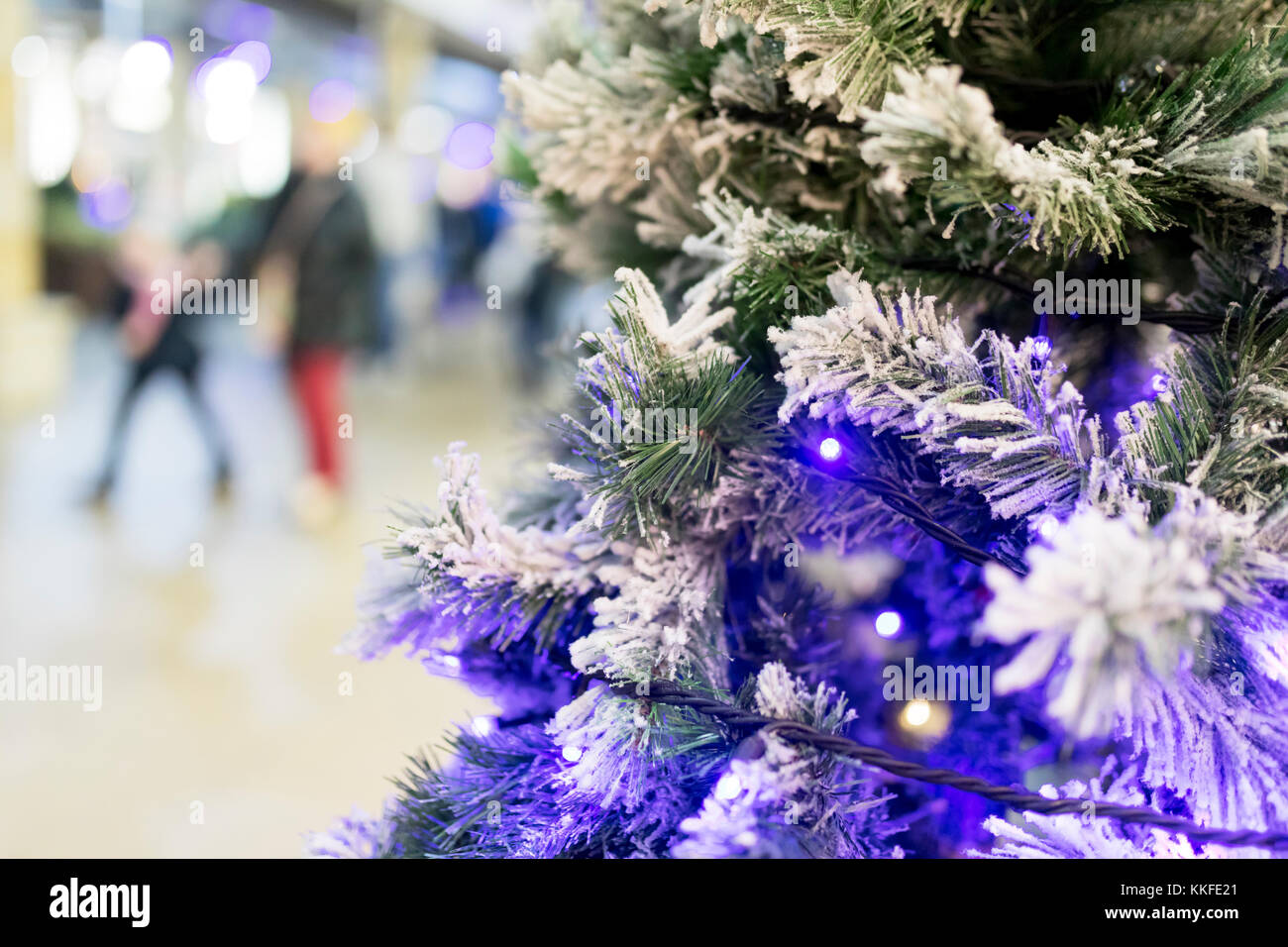 Nahaufnahme eines künstlichen Weihnachtsbaum mit blauen funkeln Lichter und Frost oder Schnee in einem Einkaufszentrum oder das Einkaufszentrum mit Menschen im b verschwommen Stockfoto