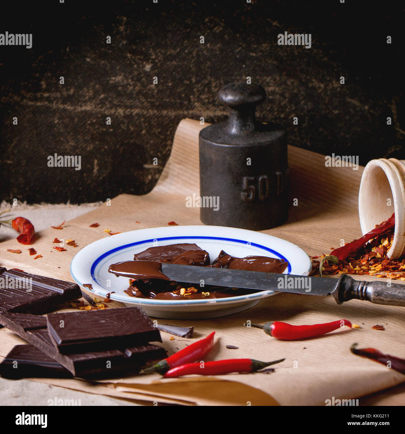 Häckseln, dunkle Schokolade mit frischen und trockenen red hot chili peppers auf Backpapier mit Teller von Heiß geschmolzene Schokolade und vintage Messer. Stockfoto