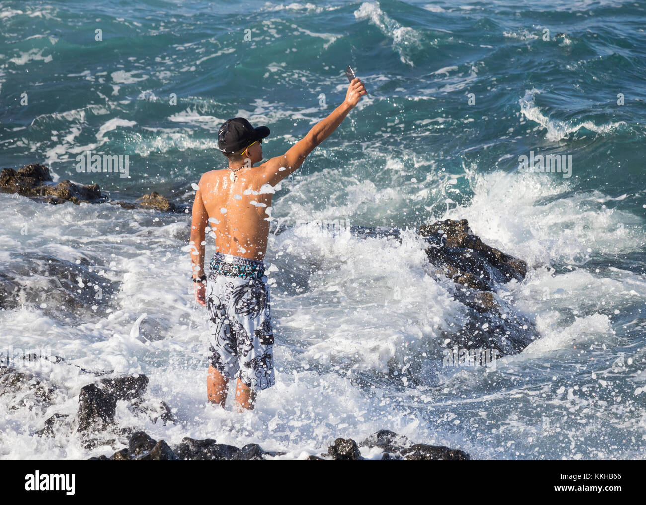 Touristische erhält eine Tiefe wie eine Welle bricht über ihn, als er konzentriert sich auf eine selfie. Stockfoto
