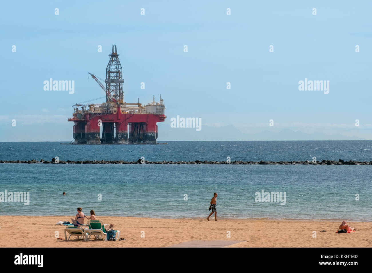 Die Leute am Strand mit Bohrplattform im Hintergrund - Stockfoto