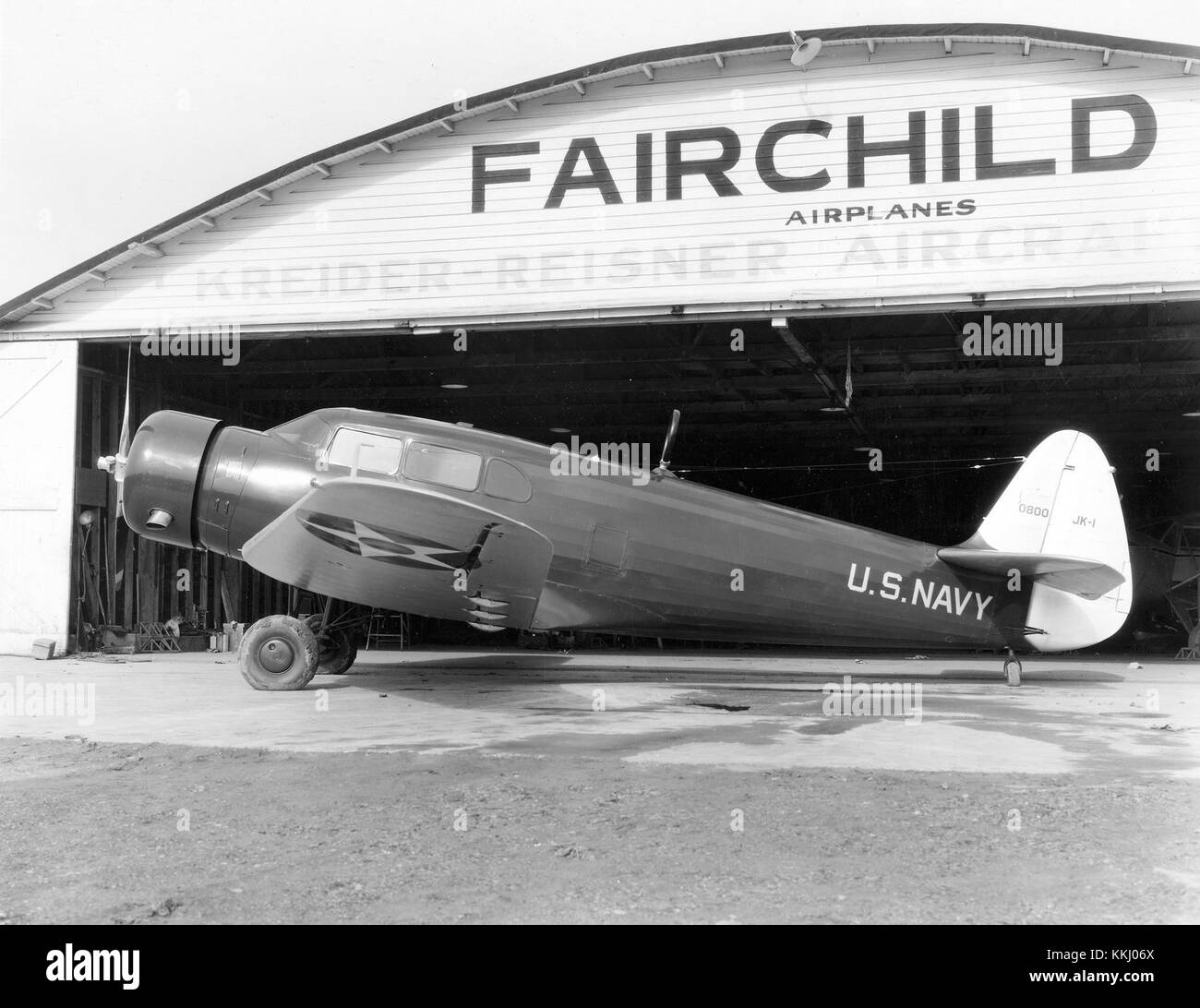 Eine linke Ansicht des Fairchild JK-1 (BuNo 0800)-Flugzeugs der US Navy, fotografiert vor einem Fairchild-Flugzeughangar um 1937 und hebt dessen Design und militärische Nutzung hervor. Stockfoto