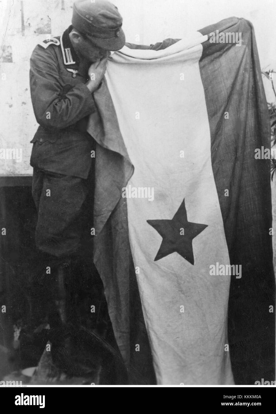 Ein historisches Foto, das einen deutschen Soldaten neben der Flagge der jugoslawischen Partisanen zeigt, das während des Zweiten Weltkriegs 1943 aufgenommen wurde. Stockfoto
