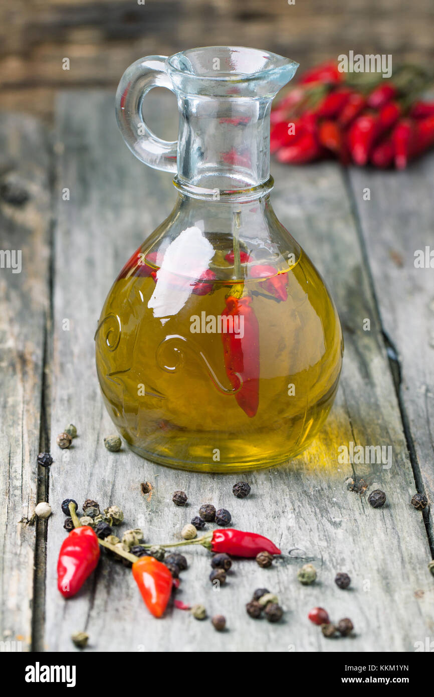 Glas Flasche Olivenöl mit red hot chili peppers über alte hölzerne Hintergrund. siehe Serie Stockfoto