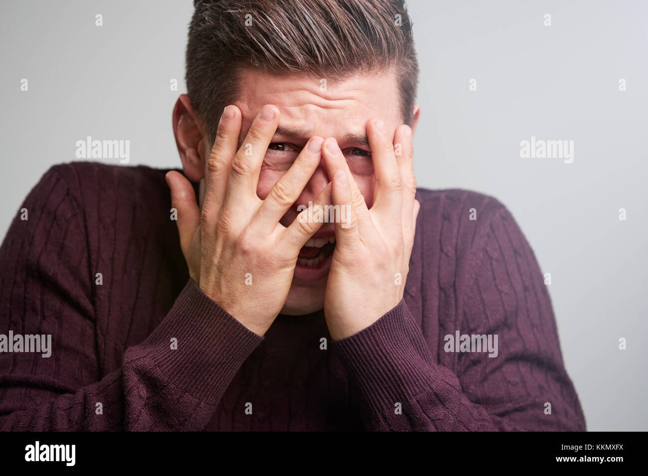 Junge weiße Mann durch seine Finger suchen Angst Stockfoto