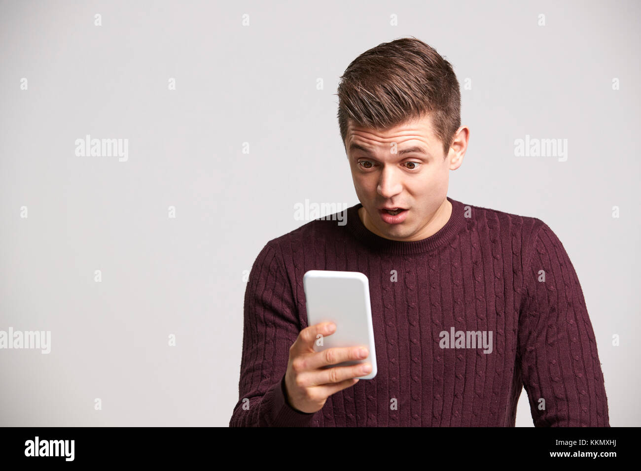 Porträt einer Schockierten jungen weißen Mann mit einem Smartphone Stockfoto