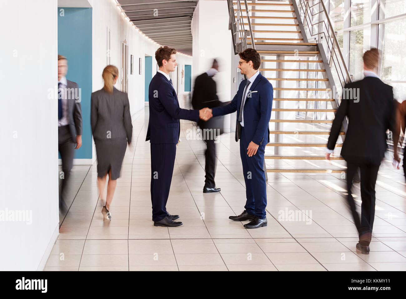 Zwei weiße Geschäftsmänner Händeschütteln in der hektischen modernen Lobby Stockfoto