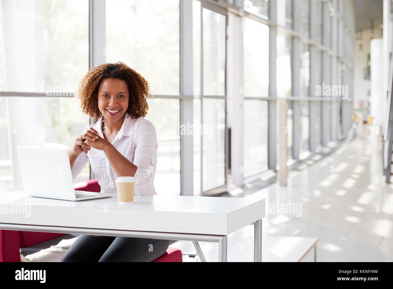 Junge Geschäftsfrau mit Laptop am Schreibtisch zu Kamera suchen Stockfoto