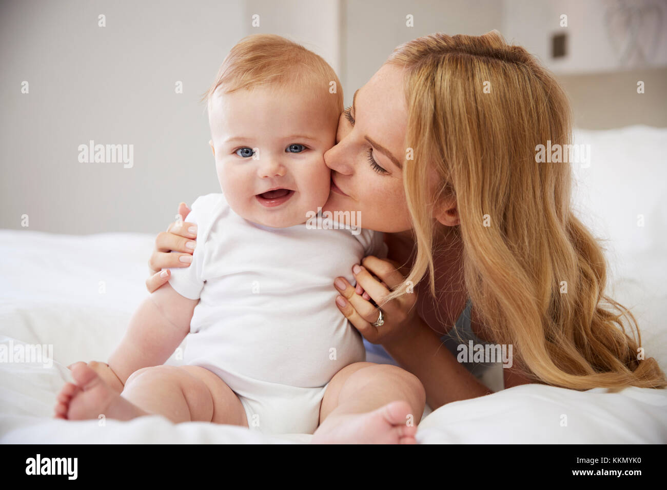 Mutter lag auf dem Bett zu Hause gibt Baby Sohn Kuss Stockfoto