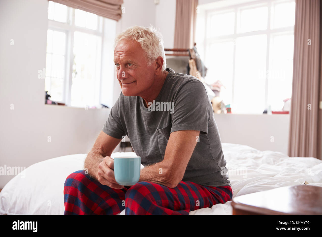 Älterer Mann sitzt auf der Seite des Bett mit heißen Getränken Stockfoto