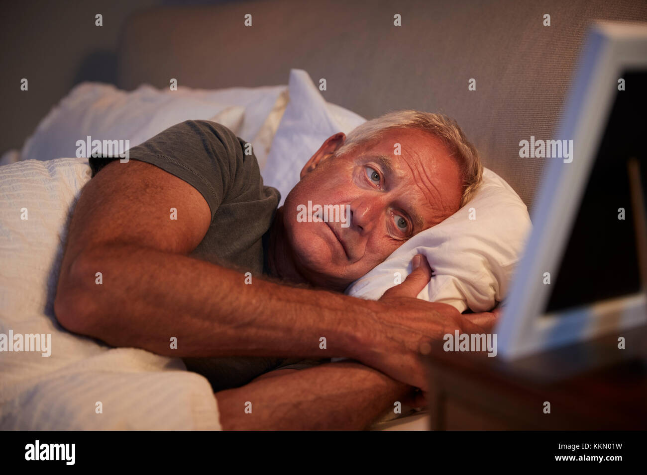 Traurig älterer Mann im Bett liegend auf der Suche nach Bilderrahmen Stockfoto