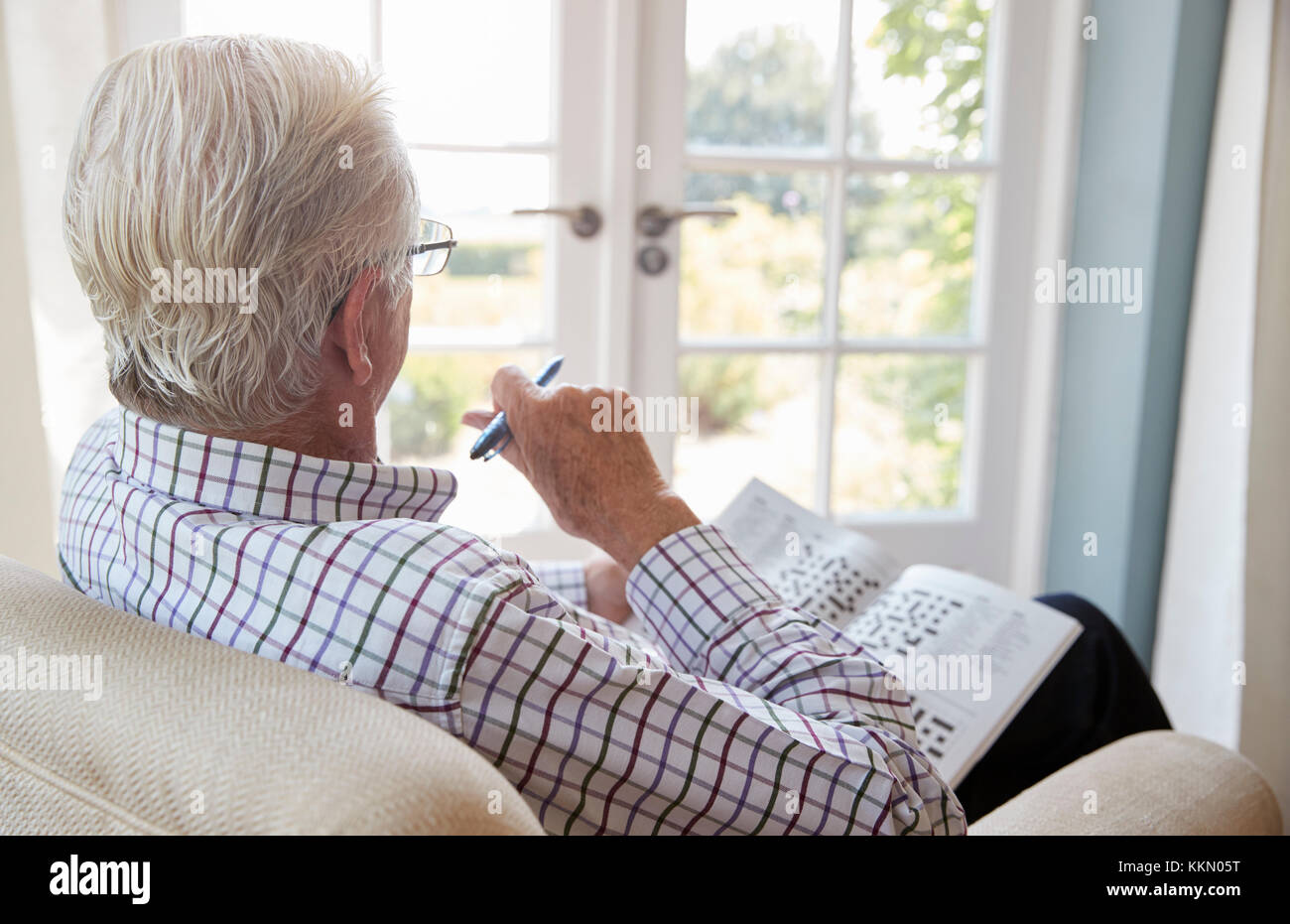 Älterer Mann sitzt in einem Sessel Kreuzworträtsel zu tun, in der Nähe Stockfoto