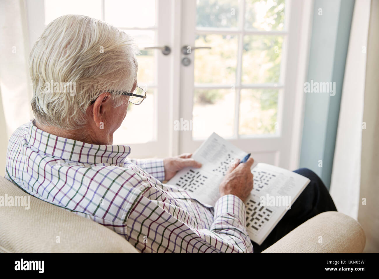 Älterer Mann sitzt in einem Sessel Kreuzworträtsel zu tun, in der Nähe Stockfoto