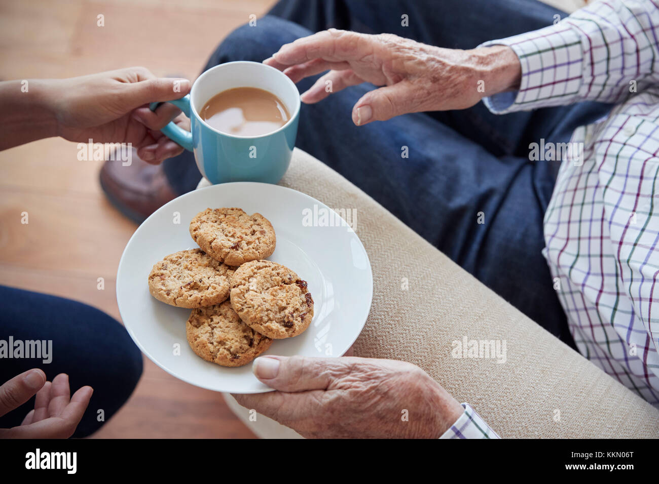 Frau übergibt Tee und Gebäck zu Sitzender älterer Mann, Detail Stockfoto