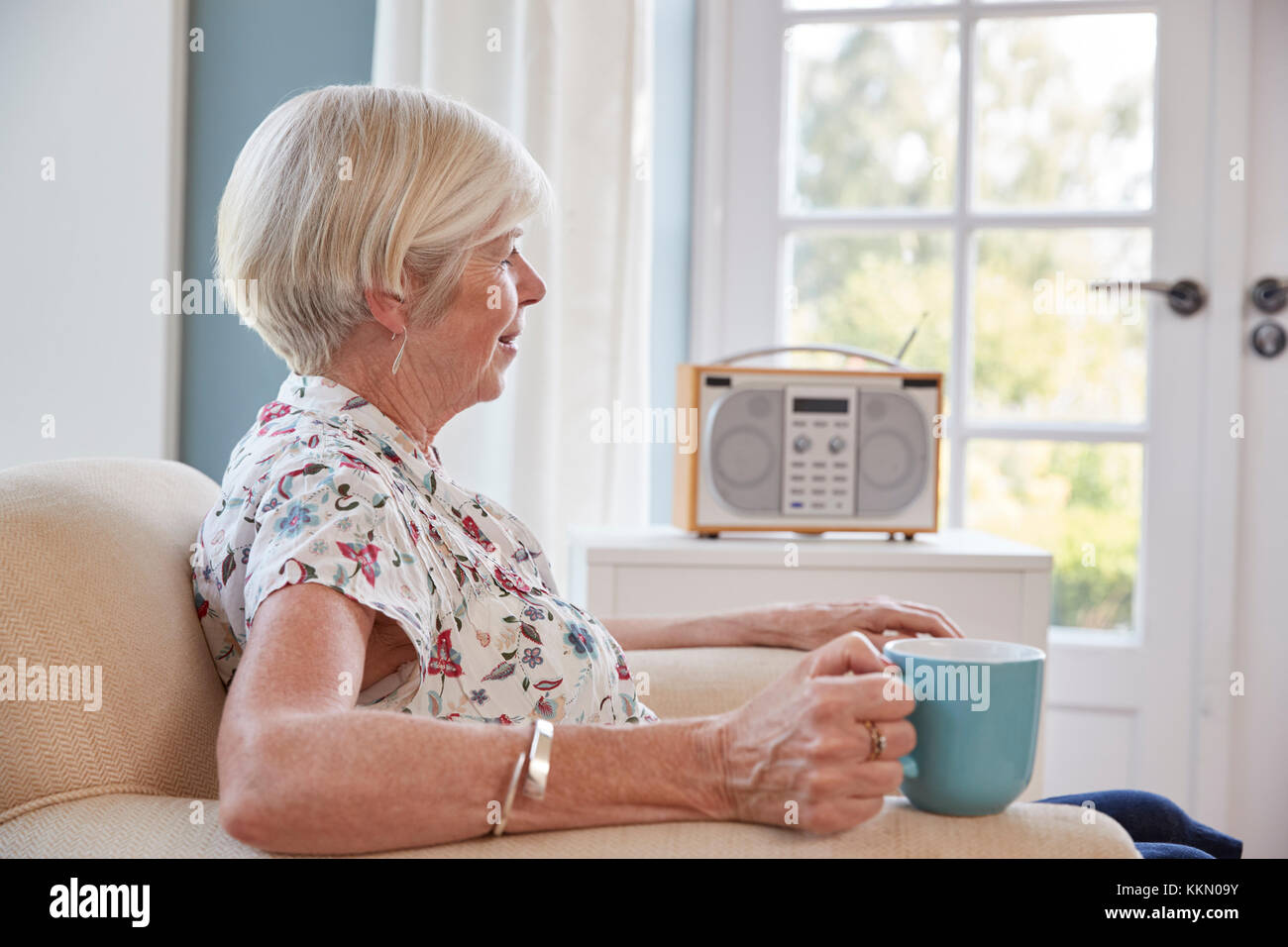 Ältere Frau trinkt Tee und Radio hören zu Hause Stockfoto