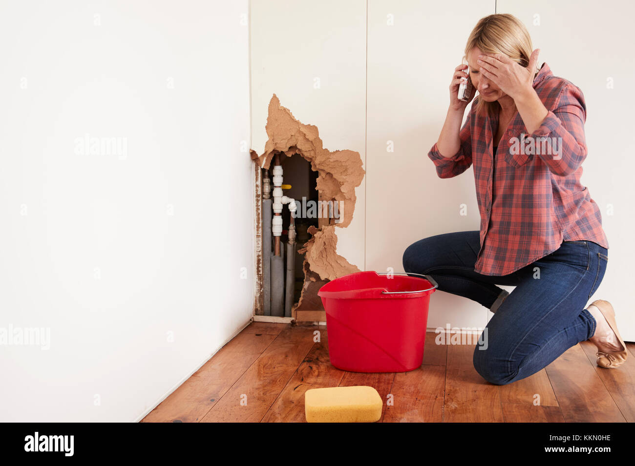 Frau mittleren Alters mit einem Wasserrohrbruch telefonieren für Hilfe Stockfoto