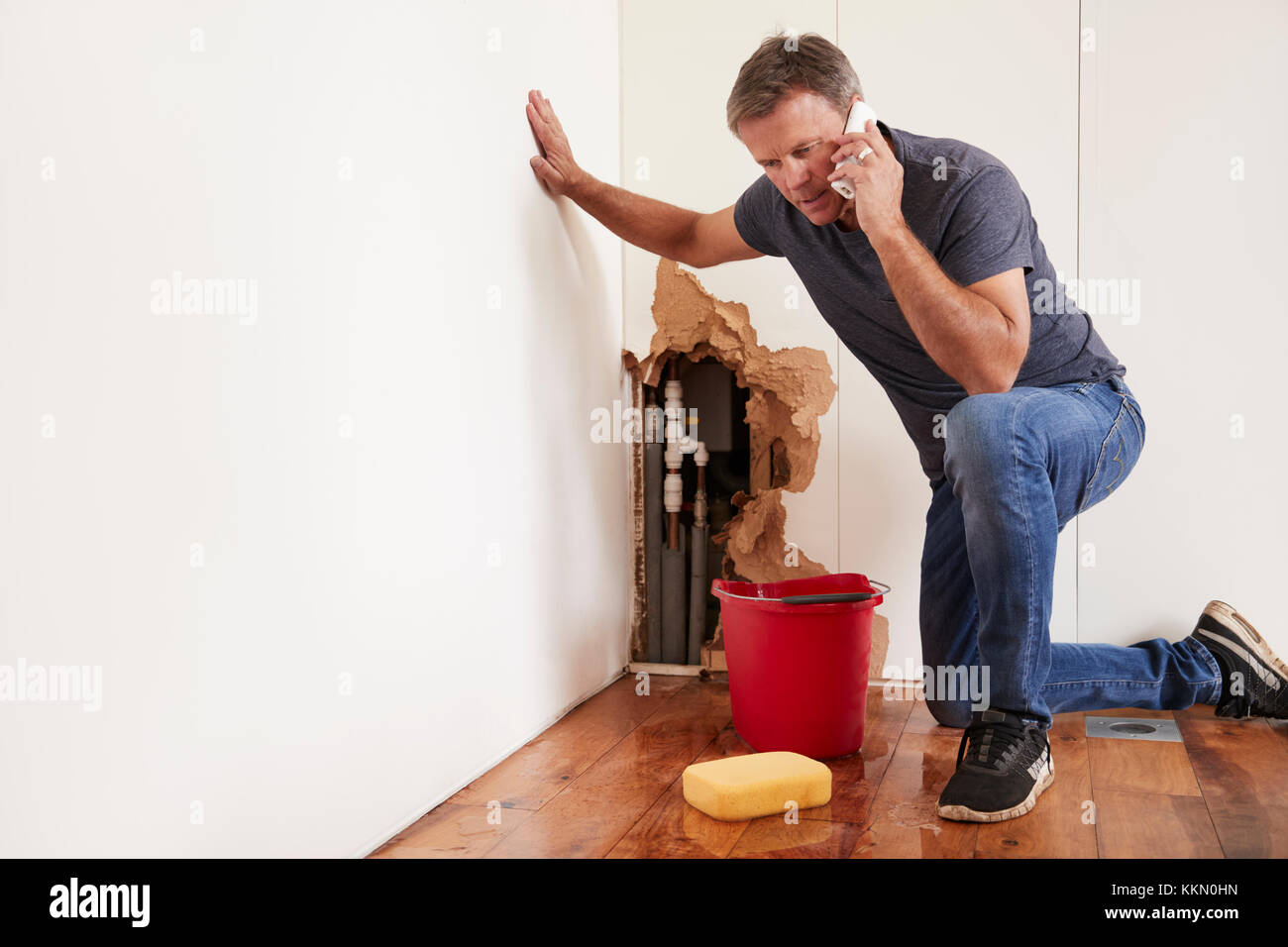 Im mittleren Alter Mann mit einem Wasserrohrbruch telefonieren für Hilfe Stockfoto