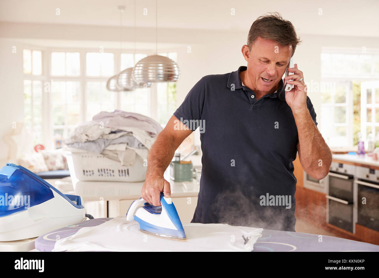 Im mittleren Alter Mann per Telefon abgelenkt beim Bügeln Stockfoto