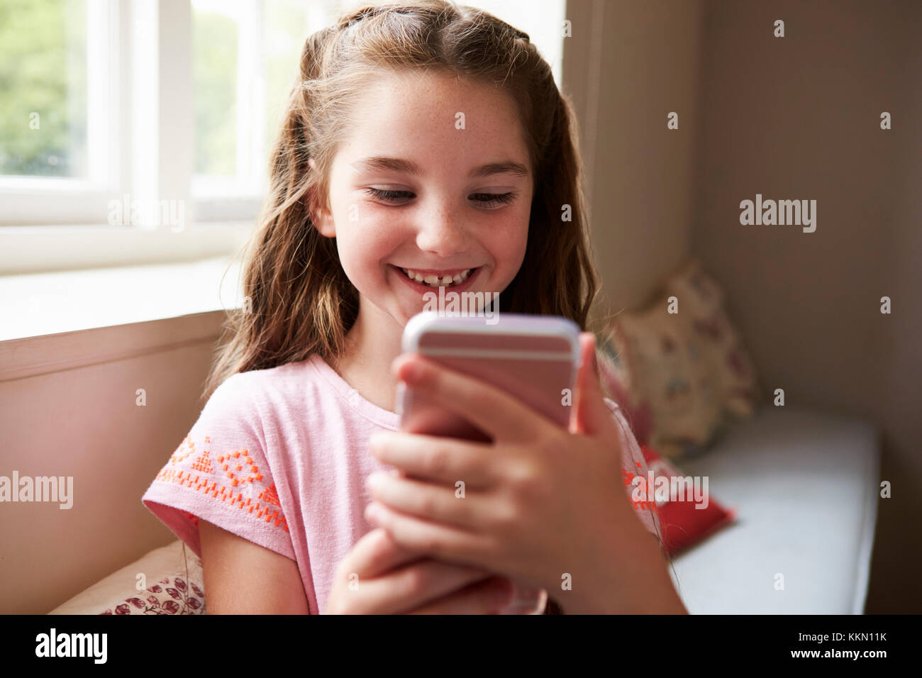 Lächelnde Mädchen sitzen auf Platz am Fenster, die Spiel am Handy Stockfoto