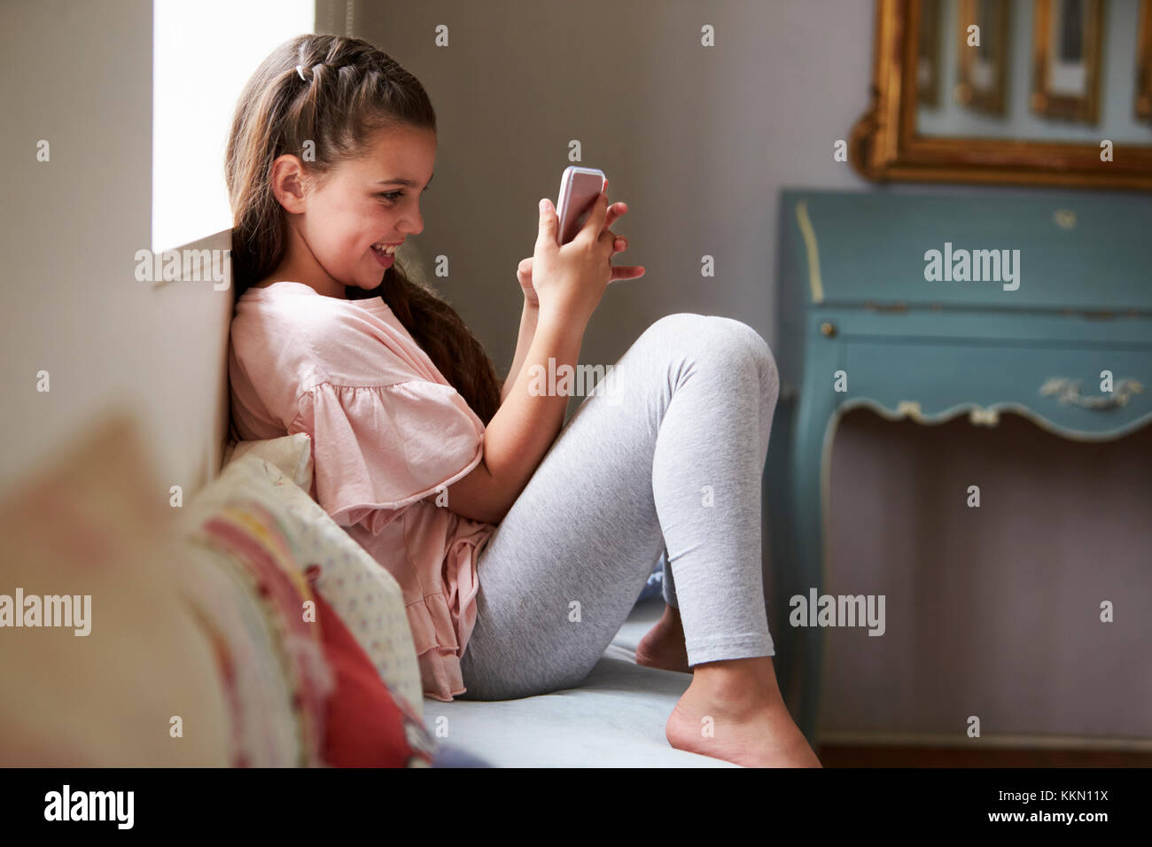 Lächelnde Mädchen sitzen auf Platz am Fenster, die Spiel am Handy Stockfoto