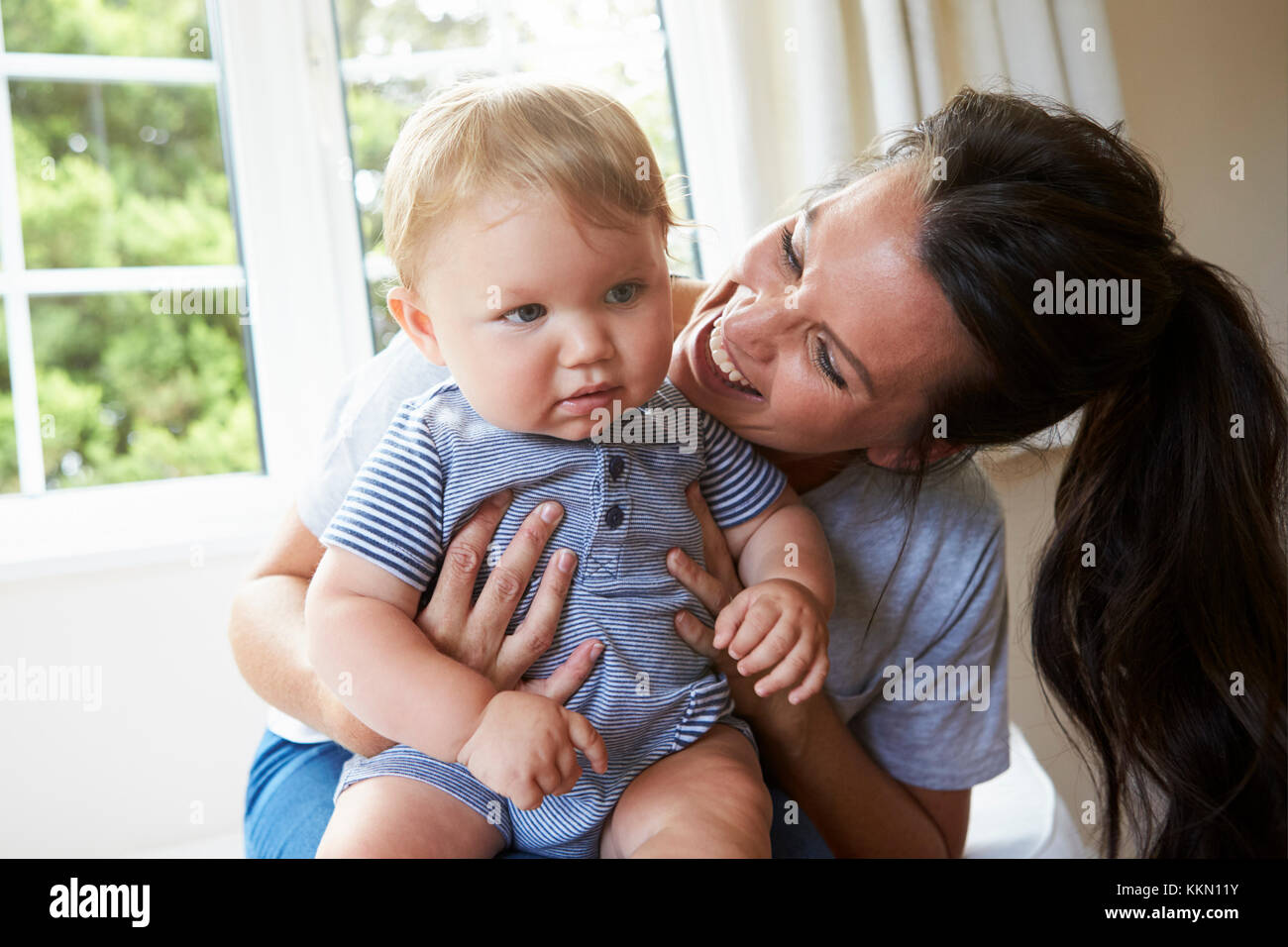 Mutter umarmt Happy Baby Sohn durch Fenster zu Hause Stockfoto