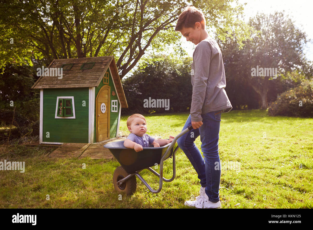 Junge Drücken kleiner Bruder im Garten Schubkarre Stockfoto