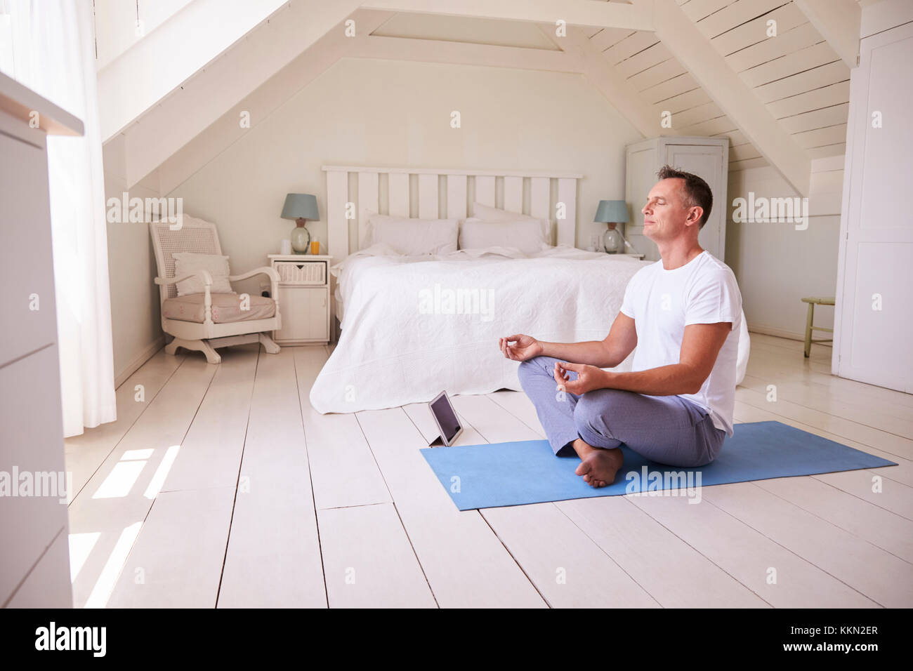 Reifer Mann mit digitalen Tablet mit Meditation App im Schlafzimmer Stockfoto