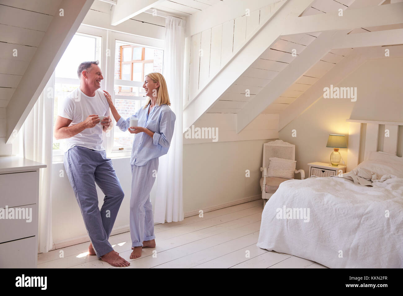 Reifes Paar stehend durch Schlafzimmer Fenster mit heißen Getränken Stockfoto
