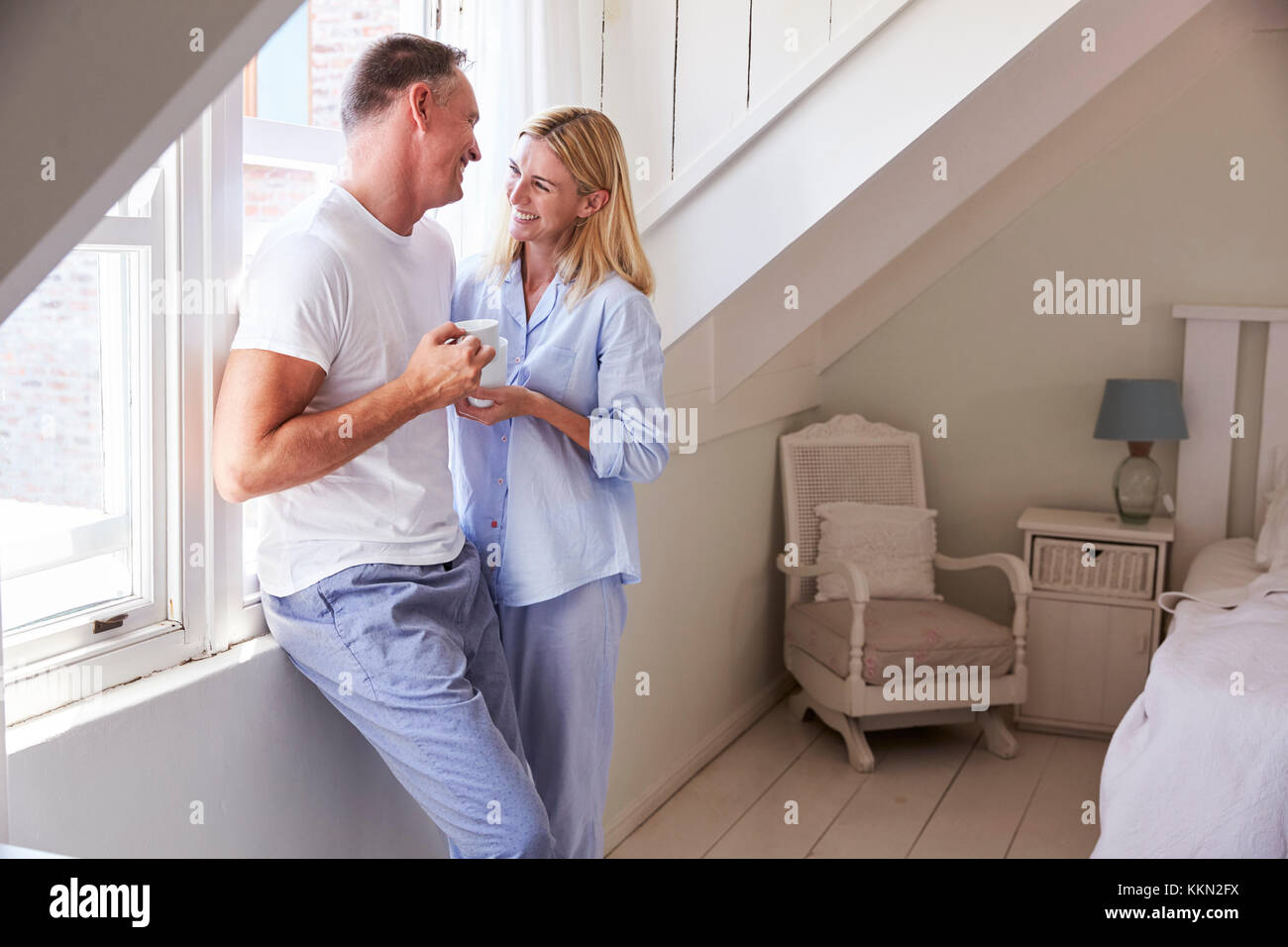 Reifes Paar stehend durch Schlafzimmer Fenster mit heißen Getränken Stockfoto
