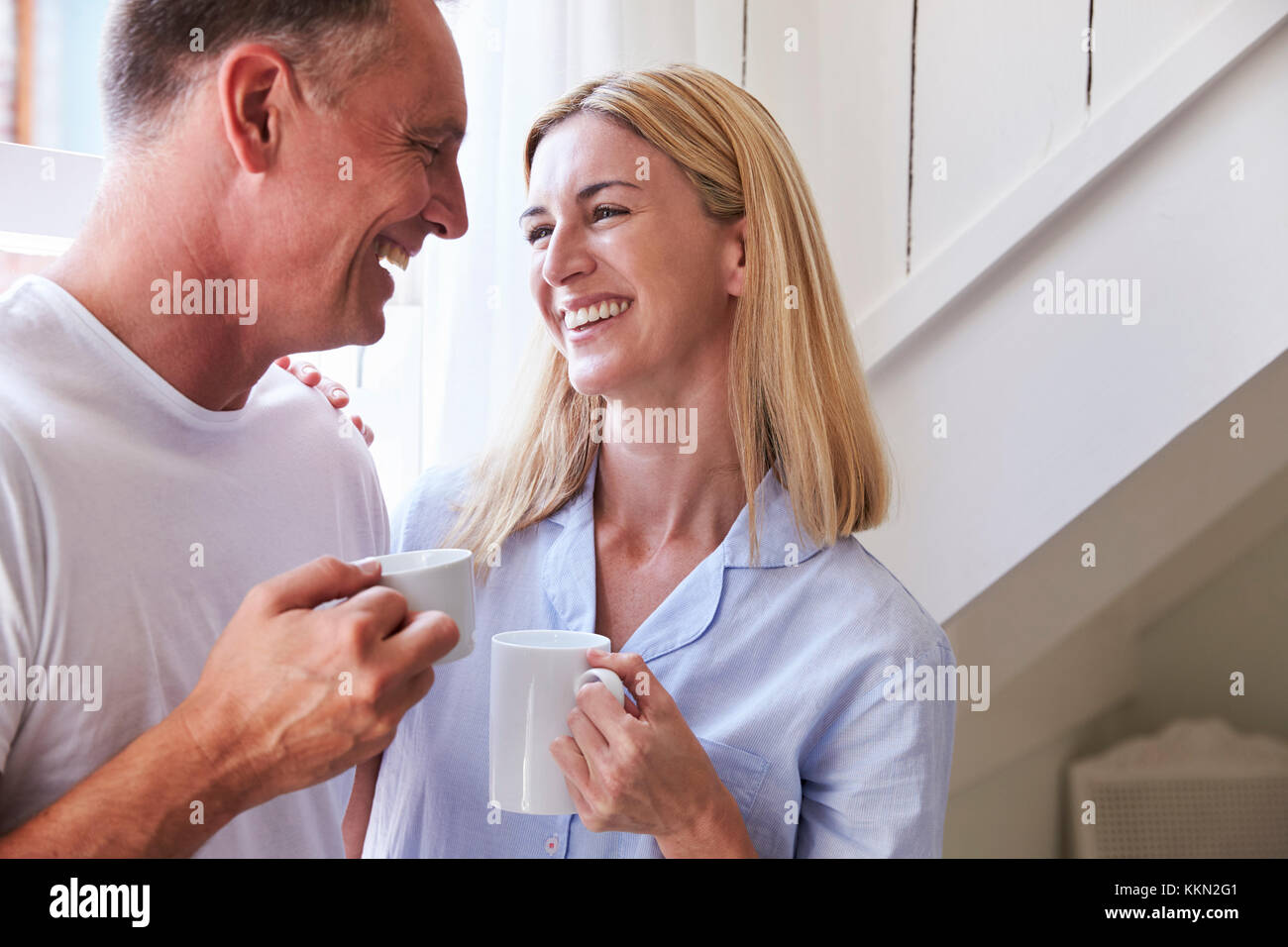 Reifes Paar stehend durch Schlafzimmer Fenster mit heißen Getränken Stockfoto