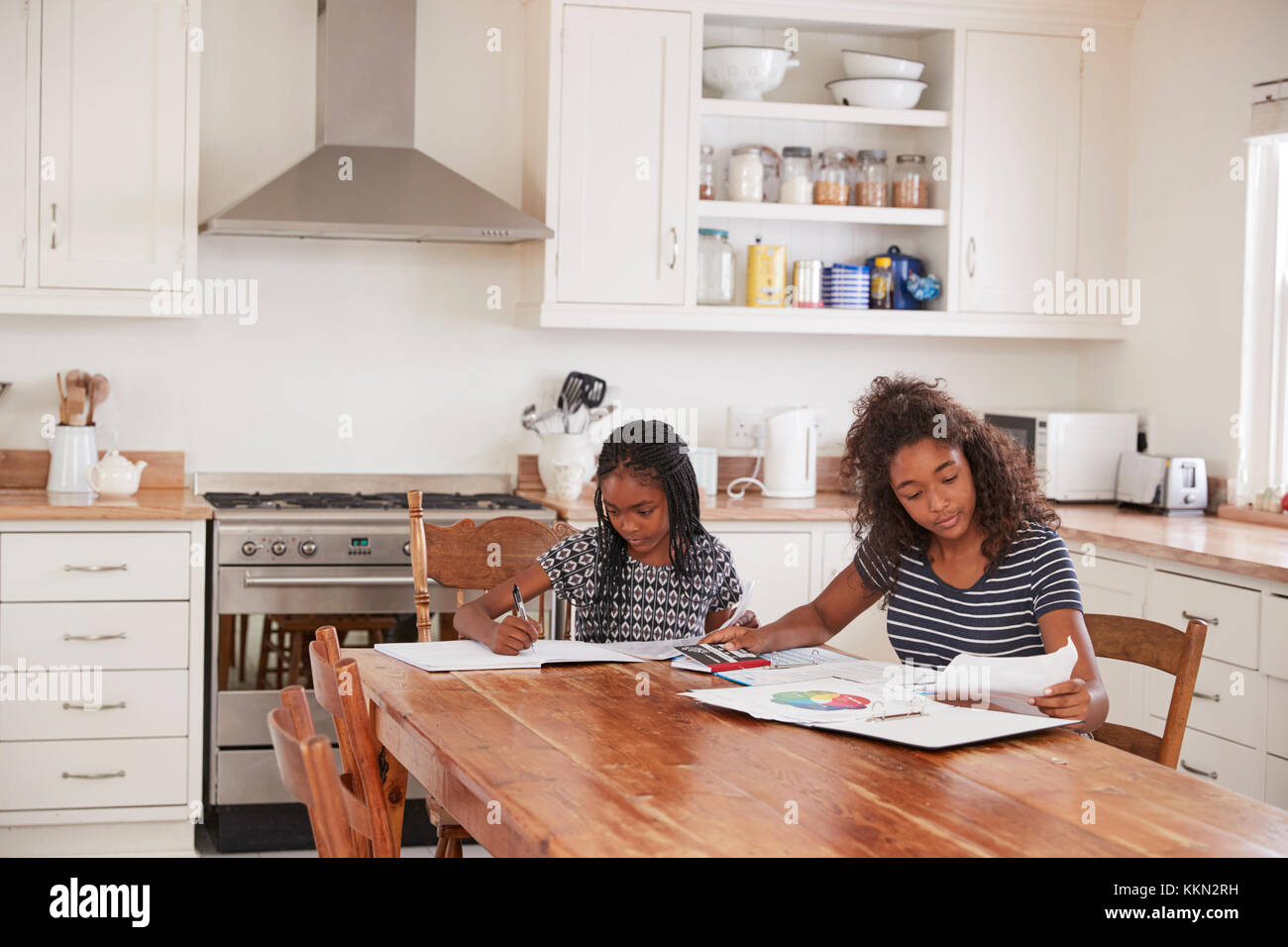 Zwei Schwestern am Tisch in der Küche Hausaufgaben sitzen Stockfoto