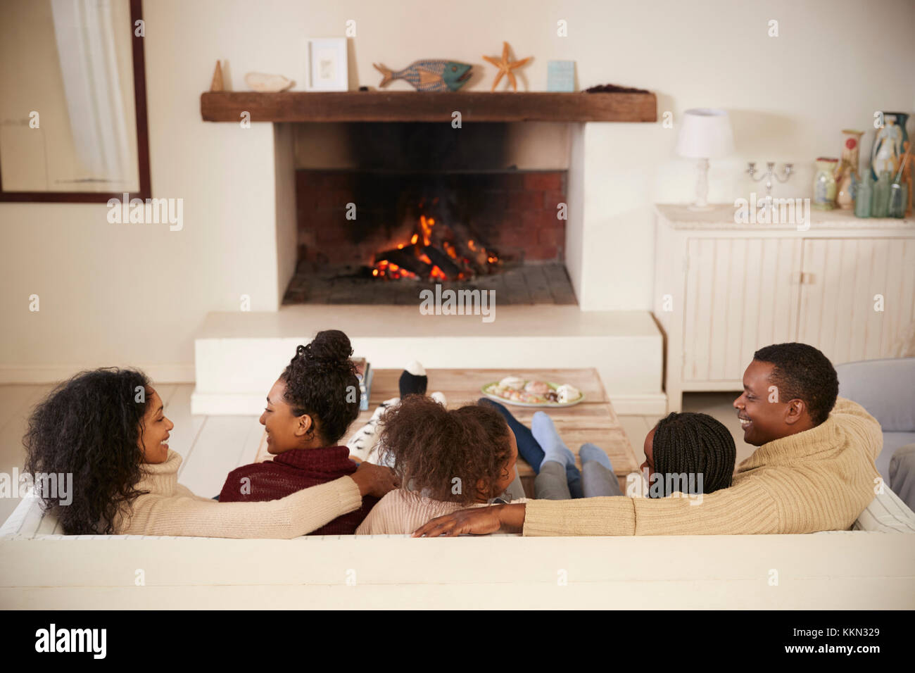Familie sitzt auf einem Sofa in der Lounge am offenen Feuer Stockfoto