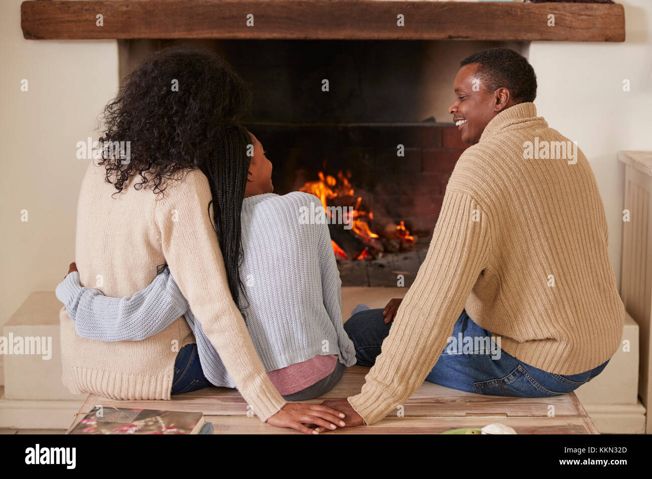 Die Eltern Sitzen mit Tochter in der Lounge am offenen Feuer Stockfoto