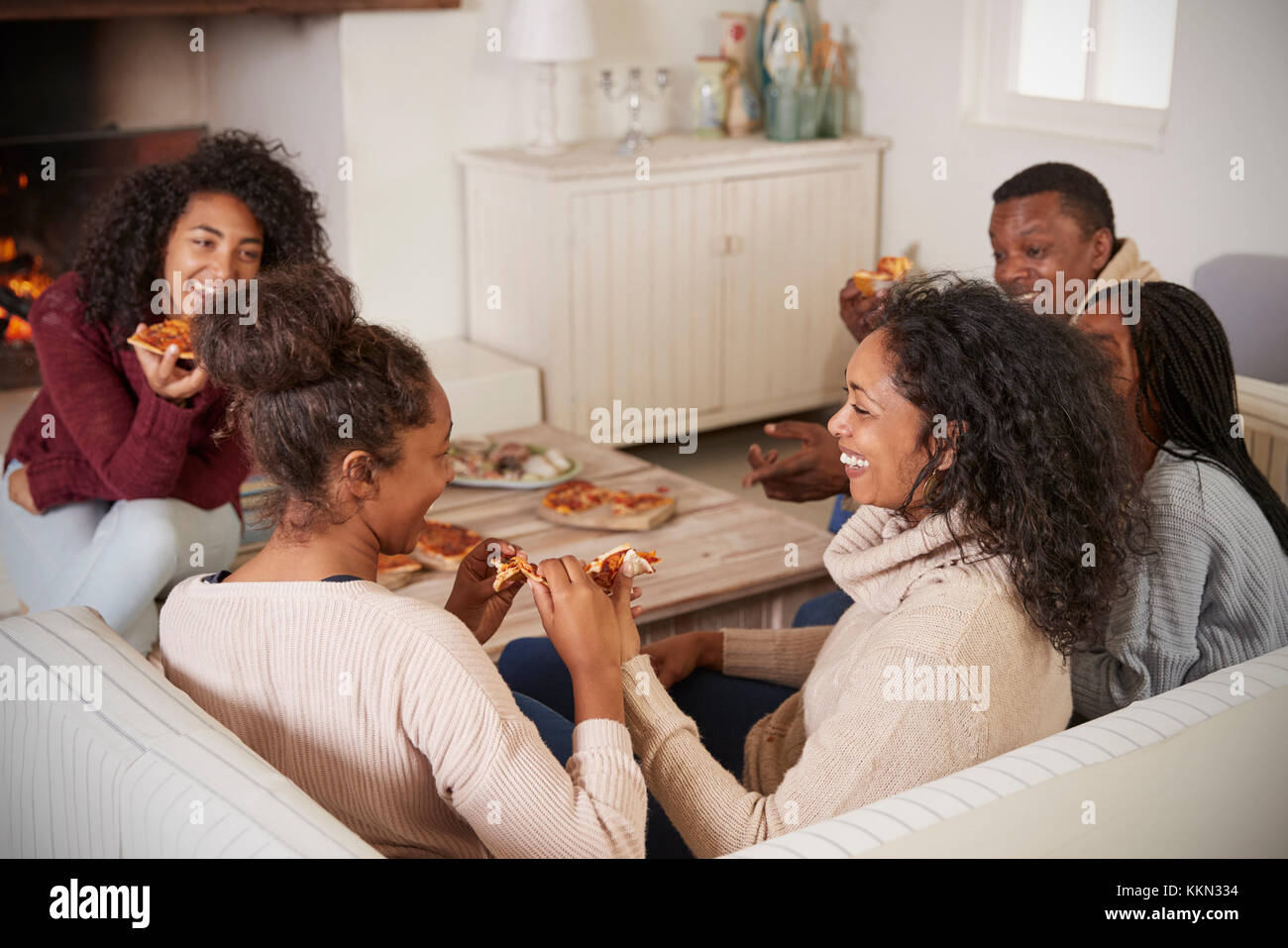 Familie sitzt auf einem Sofa in der Lounge am offenen Feuer essen Pizza Stockfoto