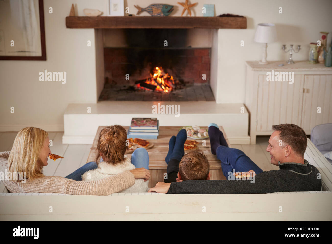 Familie sitzt auf einem Sofa in der Lounge am offenen Feuer Stockfoto