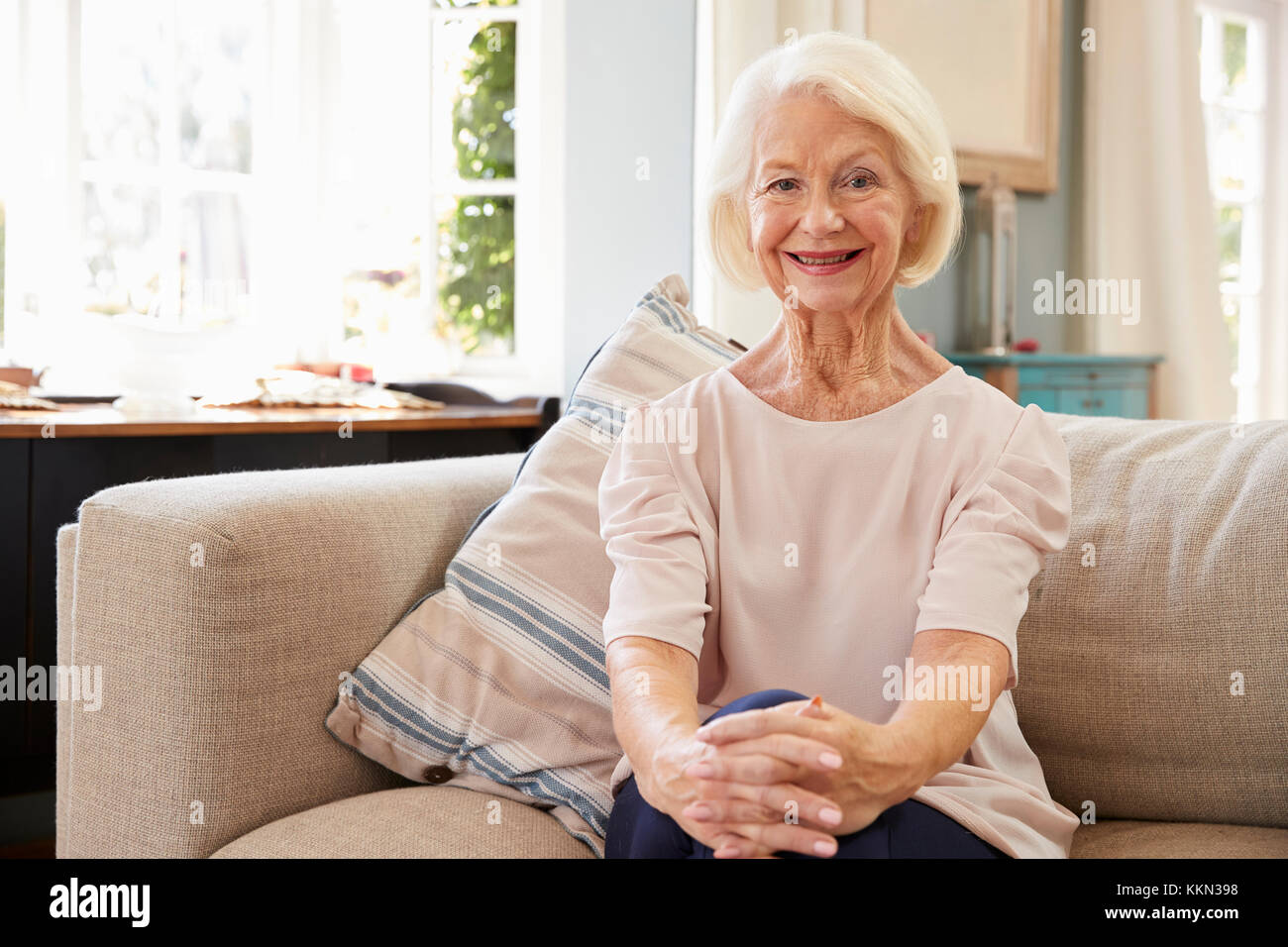 Portrait Of Smiling Senior Woman Sitting On Sofa zu Hause Stockfoto